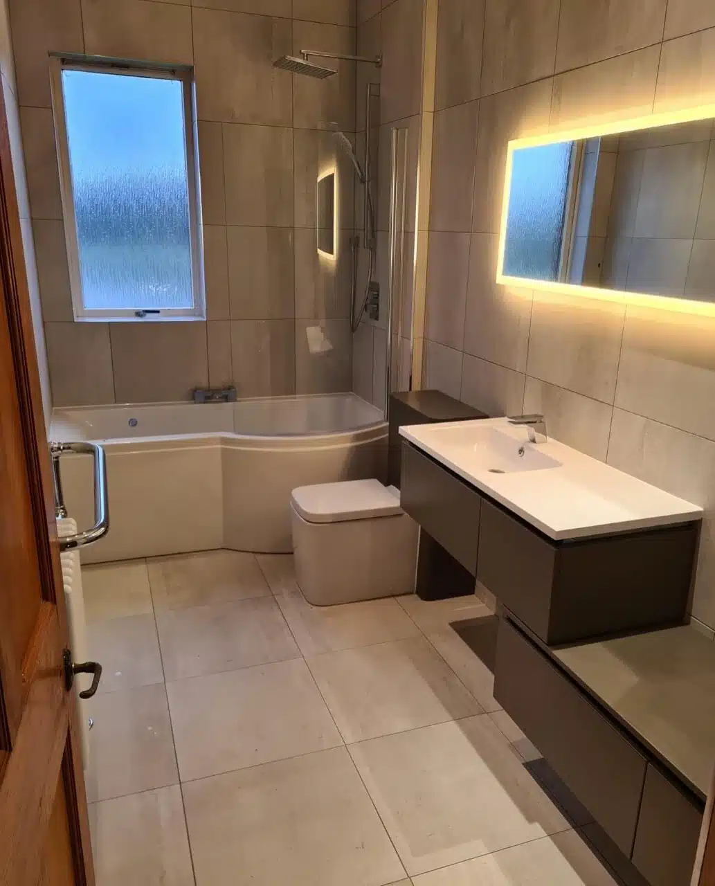 Stunning renovated bathroom newly renovated bathroom with white square tiling and grey/white units, toilet and bathtub. Vanity mirror with white back light