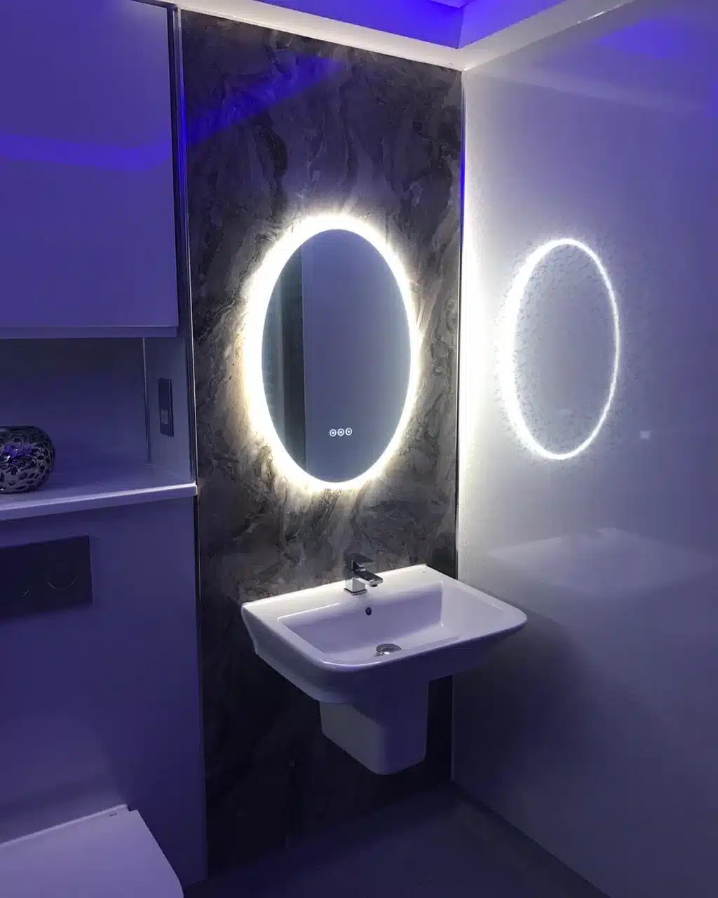 ambient bathroom renovation newly fitted bathroom showcasing a vanity mirror with white backlight. New white sink and toilet with a grey feature wall.